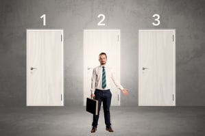 Businessman in grey room with three numbered white door behind his back